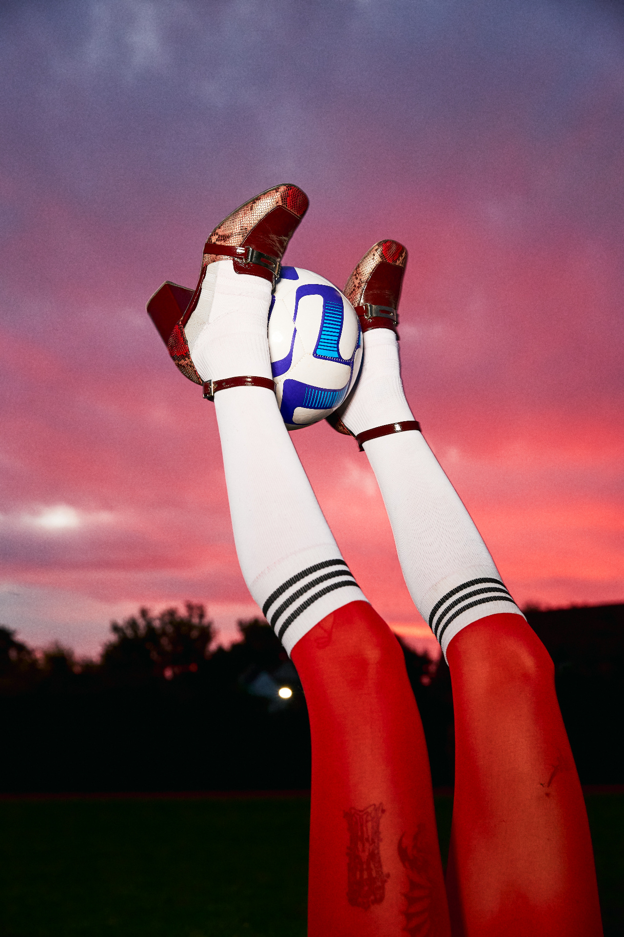 Heeled boots holding a football against a pink dusk sky