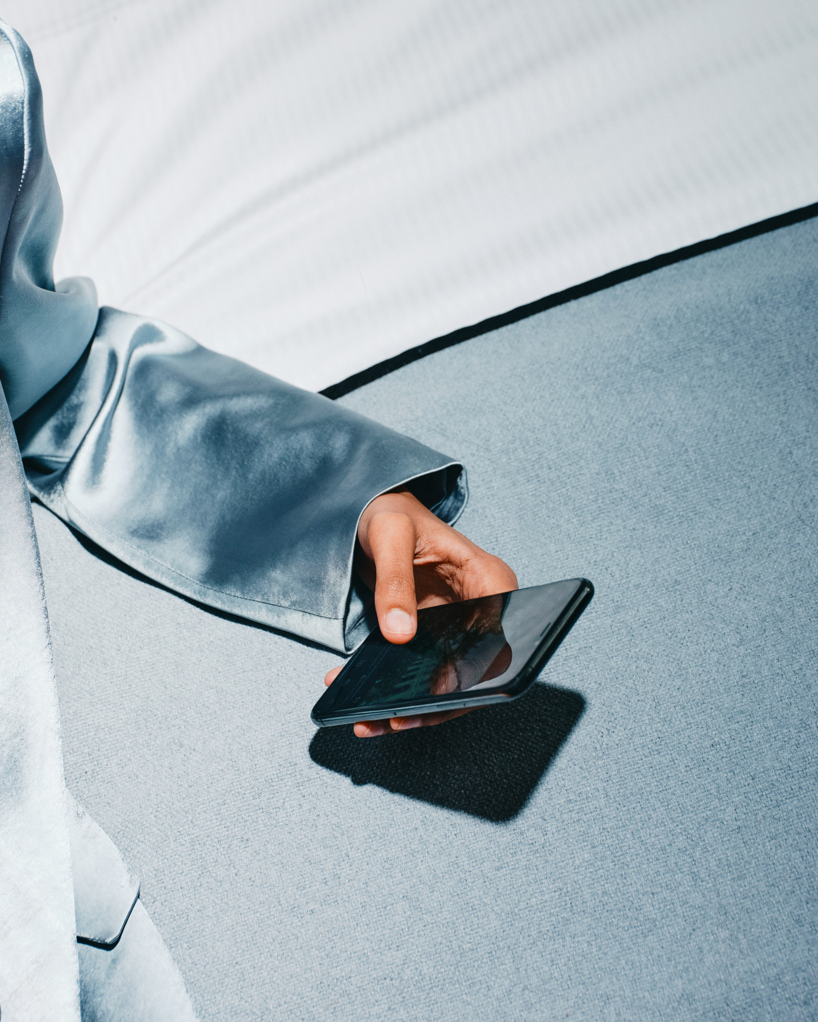 Hand in satin sleeve resting a phone on pale upholstery